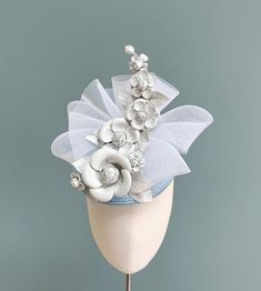 A stunning floral leather fascinator in pale blue and white. Made in pale baby blue buntal straw, this circular pillbox style percher features a sheer bow of white crinoline that offsets a beautiful and intricate spray of camellias and leaves that have been made from the softest Italian white nappa leather. Measuring 17cm, this headpiece is fitted with a fine elastic in a colour to blend in with your own hair, ensuring a close neat fit, and giving the ability to be worn at a slight forward angle Mother Of The Bride Blue Hats, Light Blue Headpieces For Royal Ascot, Elegant Spring Fascinator With Round Crown, Light Blue Headpieces For Spring Wedding, Adjustable Light Blue Mini Hat For Spring, Adjustable Light Blue Fascinator For Royal Ascot, White Handmade Flowers Headpiece For Kentucky Derby, White Spring Mini Hat Headband, Spring Wedding Mini Hat With Round Crown