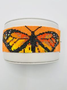 an orange and black butterfly beaded bracelet on a white wristband against a gray background