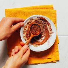 a person scooping cocoa into a bowl with a wooden spoon on a yellow napkin