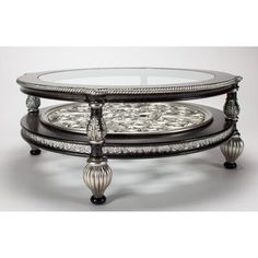 an ornately decorated coffee table with glass top and silver accents on the bottom shelf