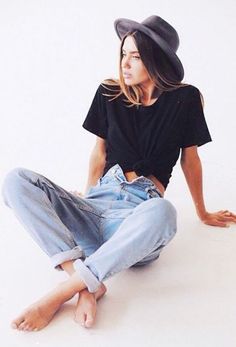 a woman sitting on the ground wearing jeans and a hat