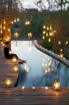 a woman sitting on a dock next to a pool filled with candles