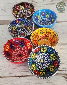 six colorful bowls sitting on top of a white wooden table with flowers painted on them