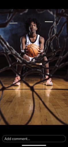 a man holding a basketball sitting on top of a wooden floor next to a net