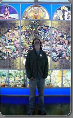 a man standing in front of a wall covered with stained glass windows and pictures on it