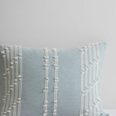 a light blue and white pillow with tassels on the front, sitting on a bed