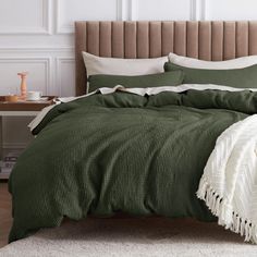 a bed with green comforter and pillows in a white walled room next to a table