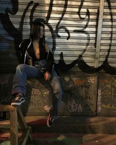 a woman sitting on top of a wooden bench in front of graffiti covered wall and door