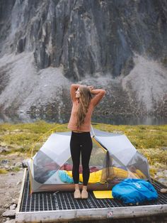 a woman standing on top of a tarp next to a tent in the mountains