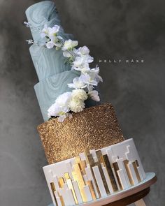 a three tiered cake with gold and white flowers on the top, sitting on a wooden stand