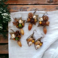 four pairs of earrings with acorns and pine cones on them sitting on a white cloth