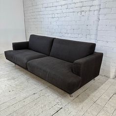 a black couch sitting in front of a white brick wall on a hard wood floor