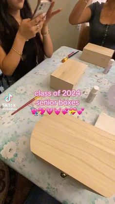 two women sitting at a table with wooden boxes on it and one woman holding a cell phone