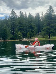 a man in a kayak is fishing on the water with trees in the background