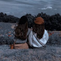 two women sitting on the grass looking at something in the distance with trees in the background