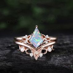 a white opal and diamond ring sitting on top of a piece of wood