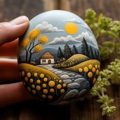 a hand holding a painted rock on top of a wooden table