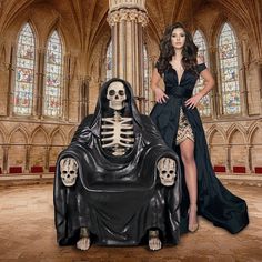 a woman standing next to a skeleton sitting in a chair