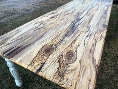 a wooden table sitting in the grass on top of a green patch of grass next to a field