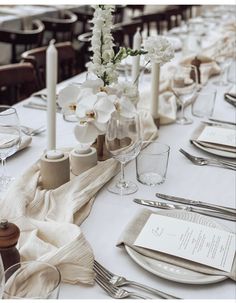 the table is set with silverware and white flowers in vases, napkins, and candles