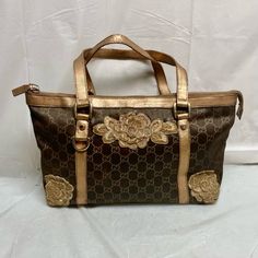 Vintage, Rare, Gucci, Gg Brown And Goldcoated Canvas With Gold Floral Embellishment Handbag (2zt0924) This Is A Pre-Owned Hand Bag Made Of Gg Brown And Gold Coated Canvas With Gold Leather Trim And Strap. It Measures 12 Inches High, 9 Inches Long And 4 Inches Wide. It Comes With A 20-Inch Strap. The Floral Embellishments Are Not Original And Was Added To Cover Some Fraying, Scuffs And Imperfections Of The Exterior. Overall It Is In Good Condition With Minimal Wear, Fading And Discoloration As Sh Floral Embellishment, Canvas Handbags, Gold Floral, Gold Leather, Hand Bag, Leather Trim, Brown Gold, Womens Tote Bags, Leather Trims