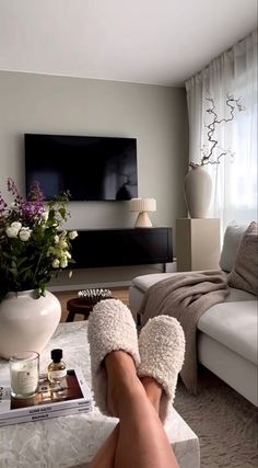 a person's feet with slippers on in front of a tv and flowers