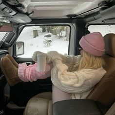 a woman sitting in the back seat of a truck holding a cup and wearing a pink hat