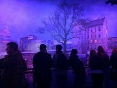 silhouettes of people standing in front of a purple and blue background with buildings on the other side