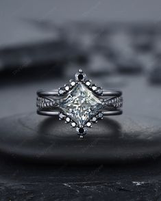 a princess cut diamond ring on top of a black stone slab with diamonds surrounding it