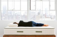 a woman laying on top of a mattress in front of a window