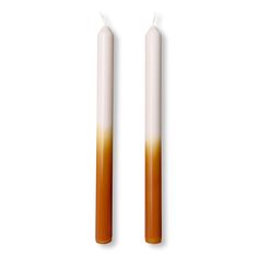 two candles that are sitting side by side on a white surface, one is orange and the other is brown