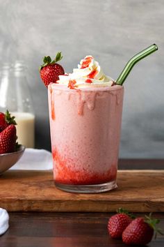 a strawberry milkshake with whipped cream and strawberries on the table next to it