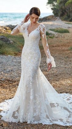 a woman in a wedding dress standing on the beach with her arms behind her head