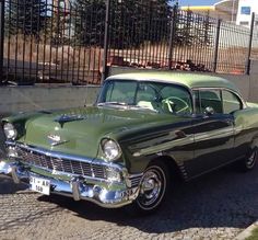 an old green car parked in front of a fence