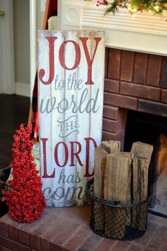 a christmas sign sitting on top of a brick fireplace next to a basket filled with presents