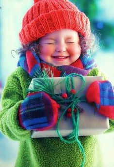 a young child holding a present wrapped in paper and wearing a red knitted hat