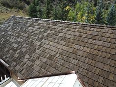 the roof of an old house with wood shingles and trees in the back ground