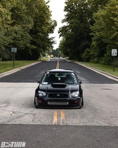 the car is parked on the side of the road with trees in the back ground