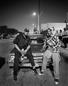 two men sitting on the hood of a car