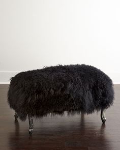 a black ottoman sitting on top of a hard wood floor next to a white wall