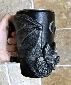 a hand holding a black mug with a bat on it's face and moon in the background