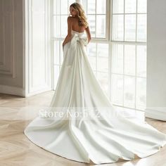 a woman in a white wedding dress standing by a window with her back to the camera