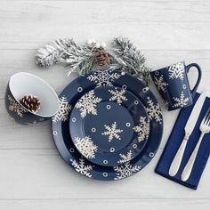 a blue and white christmas table setting with snowflakes, pine cones, and silverware