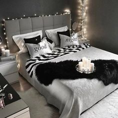 a bed with black and white pillows on it, next to a night stand filled with candles