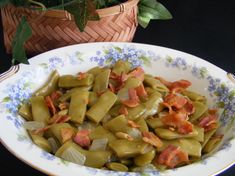 a bowl filled with green beans and bacon on top of a table next to a potted plant