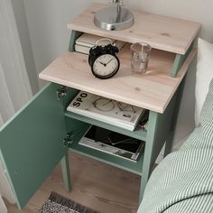 a small table with a clock on it next to a bed and a nightstand in the corner