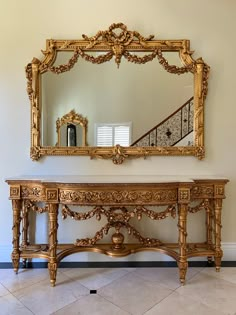 a gold console table with a mirror on top and stairs in the backround