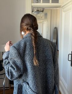 a woman standing in front of a door with her back to the camera, wearing a gray coat