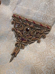 a piece of brooch sitting on top of a white and gold cloth covered in beads