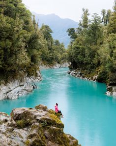 a person sitting on top of a rock next to a river